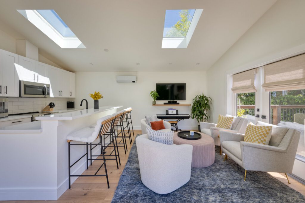 Bright living space with skylights, kitchen island seating, modern furnishings, and a wall-mounted TV above an electric piano.