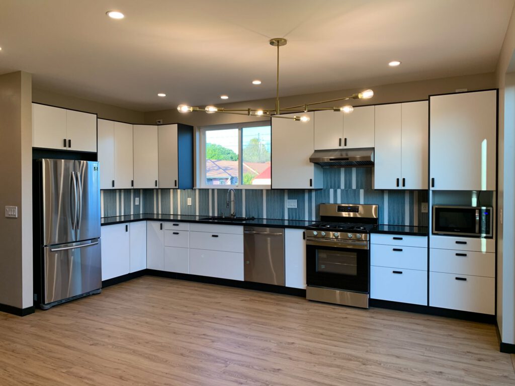 Modern kitchen with white and black cabinetry, stainless steel appliances, wood floors, and a large window above the sink.
