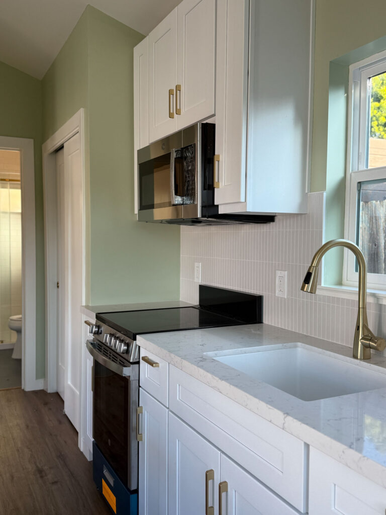 Close-up of modern kitchen with white cabinets, quartz countertops, stainless appliances, and brass fixtures.