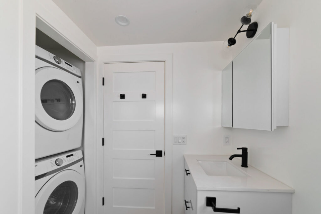 Compact laundry and vanity area with stacked washer and dryer, white cabinetry, and black hardware accents.