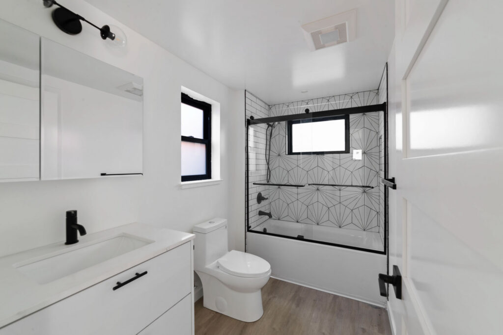 Modern bathroom with patterned tile shower, black fixtures, a white vanity, and wood-style flooring.